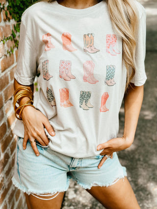 Person wearing a white t-shirt with cowboy boot designs and denim shorts.