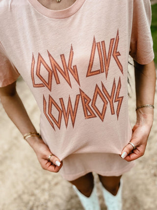 Pink t-shirt with 'Long Live Cowboys' text worn by a person outdoors.