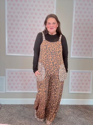Person wearing a leopard print overalls in a room with patterned wallpaper.