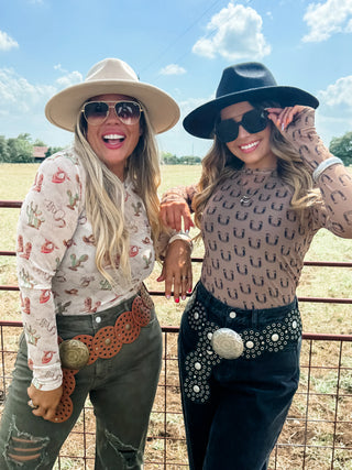 Two women in cowboy hats and sunglasses standing in a field with a fence.