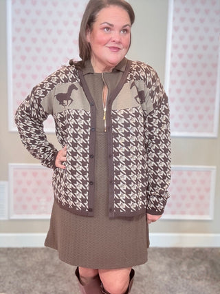 Woman wearing a patterned cardigan with horse designs in a room with pink and white checkered wallpaper.