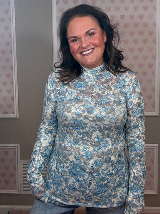 Woman wearing blue printed lace top with mock neckline and long sleeves styled with denim for feminine spring outfit.