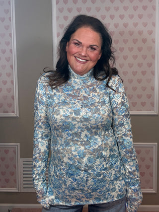 Woman wearing blue printed lace top with mock neckline and long sleeves styled with denim for feminine spring outfit.