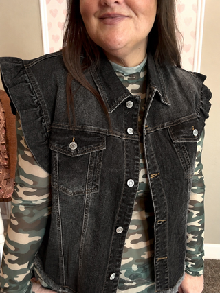 Woman wearing a faded black ruffle denim vest with Camo mesh top underneath. 