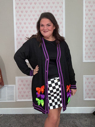 Woman wearing a black cardigan with colorful accents in a room with patterned wallpaper.