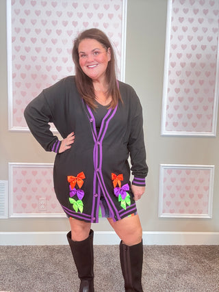 Woman wearing a black cardigan with colorful patterns in a room with heart-patterned wallpaper.