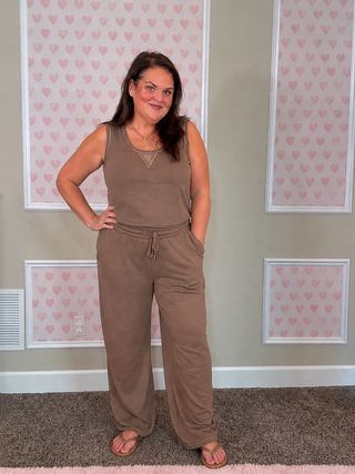 Person wearing a beige outfit with multiple pockets in a room with light-colored walls and decorative elements.