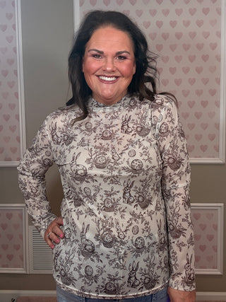 Woman wearing cream mesh top with bunny and Easter egg floral print styled with denim for festive spring outfit.