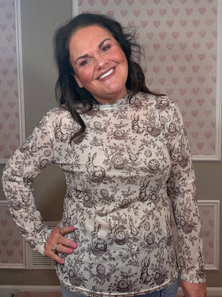 Woman wearing cream mesh top with bunny and Easter egg floral print styled with denim for festive spring outfit.