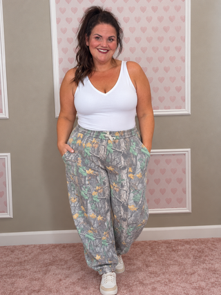 Women's Hidden Trail Camo Joggers featuring forest camouflage print, elastic waistband, functional side and back pockets, and elastic ankle hems, available in sizes S/M–3X with matching Hidden Trail Camo Pullover.