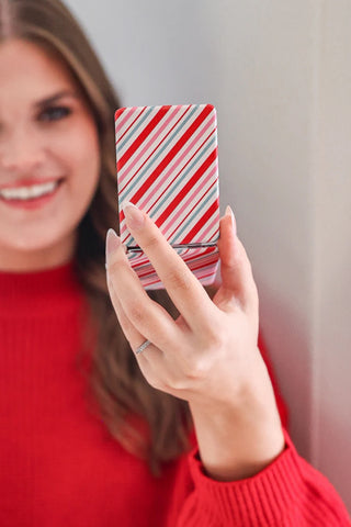 Person holding a smartphone with a candy cane pattern case against a neutral background