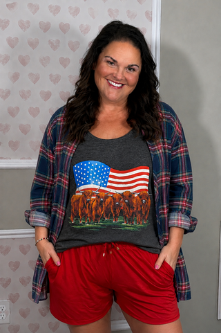 A dark heather gray racerback tank top hanging with a flannel, featuring a graphic print of Highland cows in front of a waving American flag. 