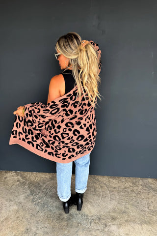 Woman wearing a taupe leopard print cardigan against a dark gray wall.