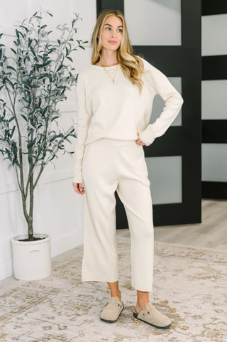 Woman in a white outfit standing in a room with a plant and black and white striped wall.