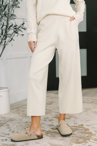 Person wearing a white outfit with wide-leg pants and beige shoes indoors.