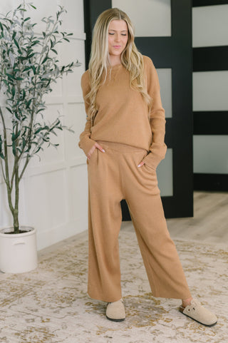 Woman wearing a brown outfit standing in a room with a plant and black and white wall.
