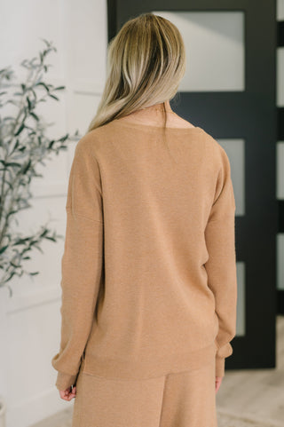 Person wearing a tan sweater and pants in a minimal indoor setting
