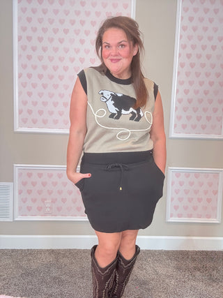 Woman wearing a sleeveless top with a cow design and black skirt in a room with heart-patterned wallpaper.