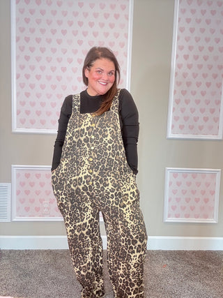 Person wearing leopard print overalls in a room with heart-patterned wallpaper.
