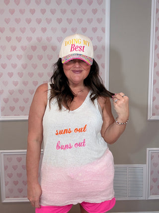 Person wearing a tank top with text and a cap in a room with heart-patterned wallpaper.