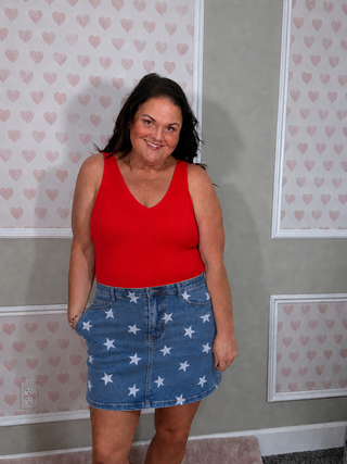Curvy woman in a flattering blue V-neck tank bodysuit paired with a denim star print skirt, styled for a chic patriotic summer outfit.