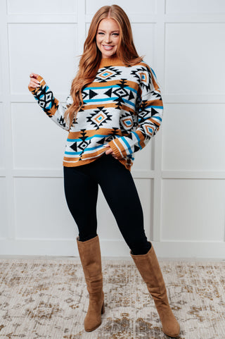 Woman wearing a patterned sweater and brown boots against a white wall.
