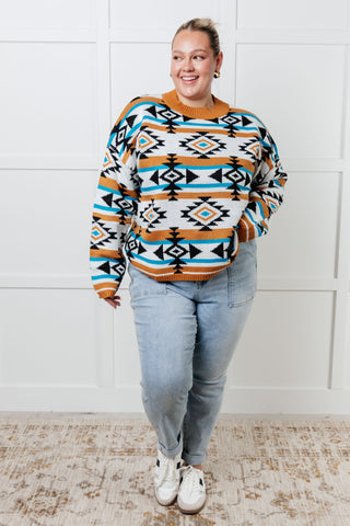 Person wearing a patterned sweater and jeans standing against a white wall.