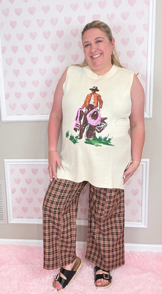 Person wearing a sleeveless top with a graphic design and plaid pants in a room with heart-patterned wallpaper.