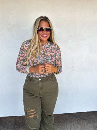 Woman wearing a floral shirt and green jeans against a white wall