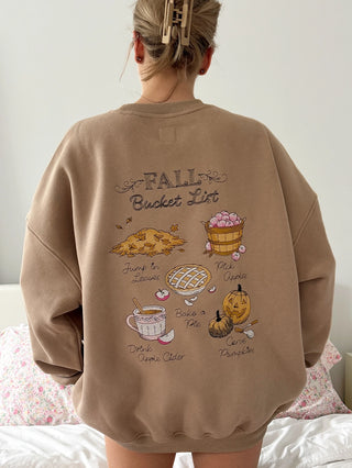 Person wearing a brown sweatshirt with 'Fall Bucket List' design on the back.