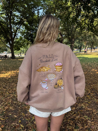 Person wearing a brown sweatshirt with fall-themed graphics in a park.
