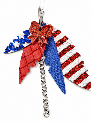 Patriotic-themed earrings featuring red, white, and blue lightning-bolt charms, a red glitter bow, and a silver metal chain on a white background.