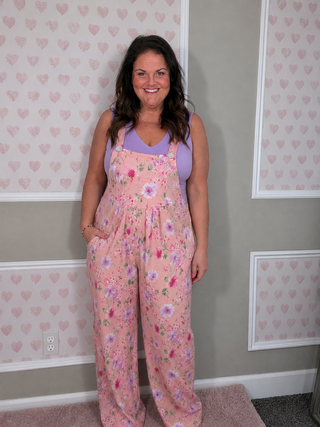Woman wearing a pink floral overalls in a room with heart-patterned wallpaper.