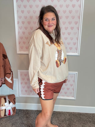 Woman wearing a beige sweatshirt with a graphic design and brown shorts in a room with heart-patterned wallpaper.