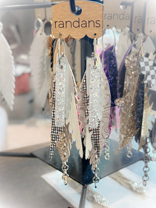 Long ivory and white layered earrings featuring glitter faux leather, textured white elements, rhinestone mesh, and silver chain dangles. Elegant and neutral with sparkle. Displayed on a “randans” card.