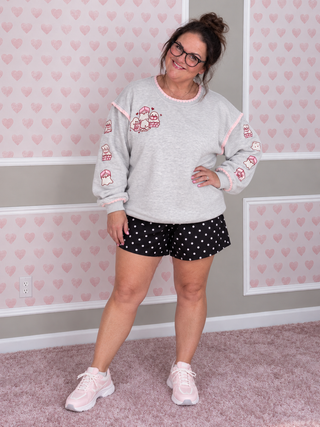 Embroidered grey sweatshirt with white and pink ghosts with books paired with black and white polka dot shorts. 
