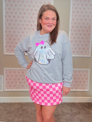 Person wearing a gray hoodie with a cartoon design and pink checkered shorts in a room with heart-patterned wallpaper.