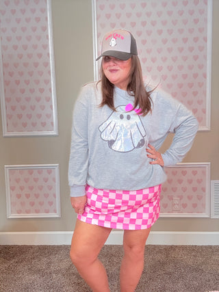 Person wearing a gray sweatshirt with a cartoon design and a pink checkered skirt in a room with heart-patterned wallpaper.