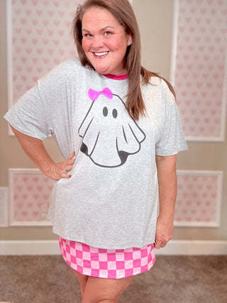 Person wearing a white t-shirt with a ghost design and pink shorts in a room with heart-patterned wallpaper.