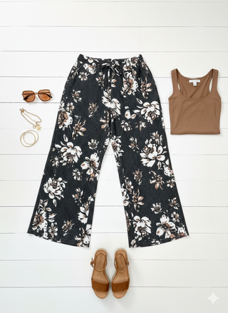 Floral pants, tank top, sandals, and sunglasses on a white wooden floor.