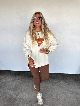 Soft oversized crew pullover with embroidered Highland cow on front, exposed seams, ribbed trim, and split cuff detail — cozy sweatshirt feel with western charm.