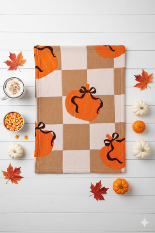 Checkered towel with pumpkins on a white wooden surface with fall decorations.