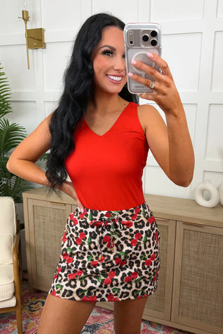 Woman taking a mirror selfie wearing a red top and patterned skirt in a home setting.