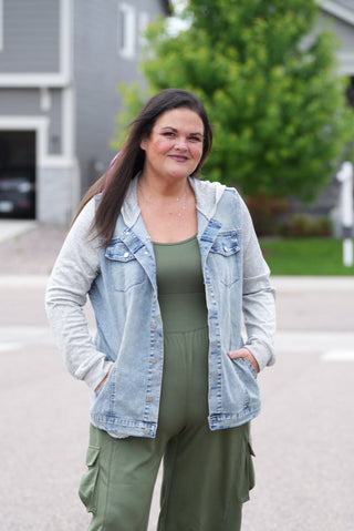 Woman in army green jumpsuit and light blue denim jacket standing on a street.