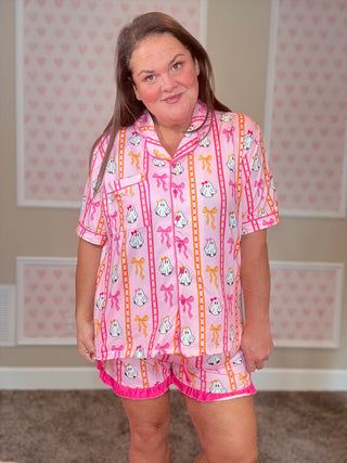 Woman wearing a pink pajama set with cartoon characters in a room with heart-patterned wallpaper.