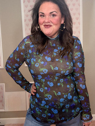 Woman wearing a sheer long-sleeve top with blue floral pattern indoors.