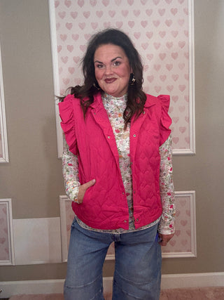 Woman wearing a pink vest over a patterned shirt with a neutral background