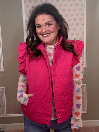 Woman wearing a pink quilted vest over a colorful heart-patterned shirt.