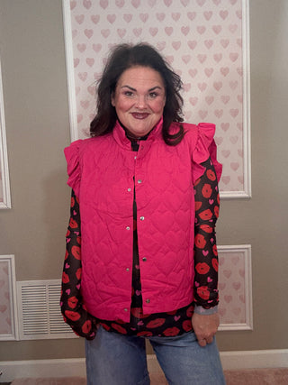Person wearing a pink quilted vest over a black and red floral dress indoors.