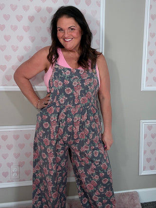 Woman in denim floral overalls posing against a wall with heart patterns